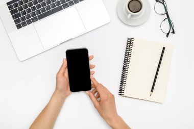 Kadın beyaz ofis üzerinde boş ekranlı akıllı telefon kullanıyor.