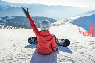 Snowboardcu kız dağlarda kayak tahtasında oturur.