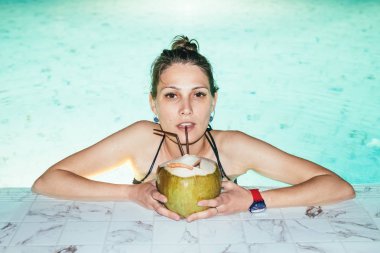 Geceleri yüzme havuzunda kokteyl içen çekici bir kadının portresi.