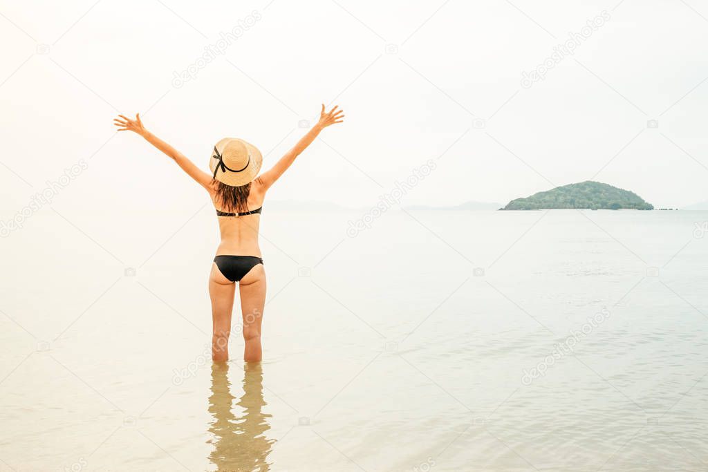 Beach vacation. Beautiful woman in sunhat and bikini standing at the beach enjoying looking view of ocean on summer day