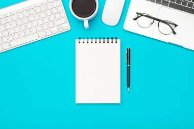 Boş defter sayfası ve dizüstü bilgisayarı olan beyaz tasarımcı ofis masası. Üst Manzara. Düz yatıyordu