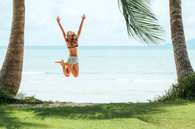 Kumsalda zıplayan mutlu genç bir kadın. Arka plan