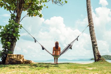 Yaz tatili konsepti. Siyah bikinili mutlu kadın tropik plajda hamakta dinleniyor.