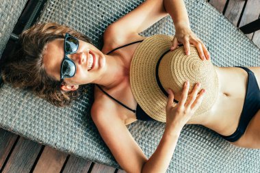 Siyah bikinili güzel bir bayanın havuz kenarındaki iskemlede rahatlarken görüntüsü.