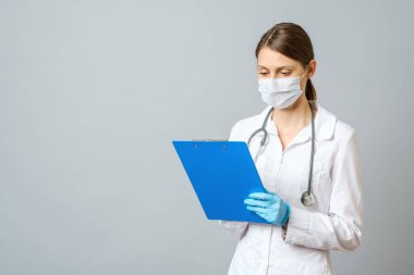 Steteskoplu genç bir kadın doktor hastaya reçete yazıyor. Not panosunda kalem tarifi olan kadın bir doktor. Gri renkte izole edilmiş