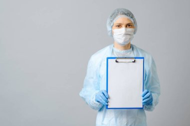 Koruyucu maske takan kadın doktor beyaz kağıtlı panoyu gösteriyor. Gri renkte izole edilmiş