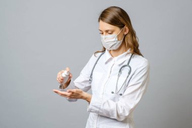 Doktor elinde bir şişe alkol spreyi tutuyor. Doktor antiseptik jel kullanmamızı tavsiye ediyor. Gri renkte izole edilmiş