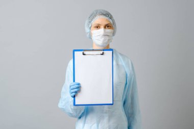 Koruyucu maske takan kadın doktor beyaz kağıtlı panoyu gösteriyor. Gri renkte izole edilmiş