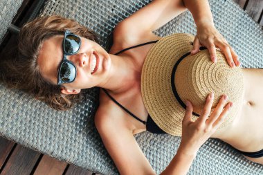 Siyah bikinili güzel bir bayanın havuz kenarındaki iskemlede rahatlarken görüntüsü.