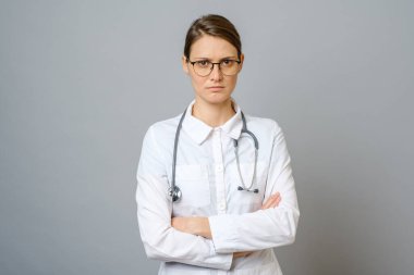 Steteskopla kameraya bakan ciddi bir doktorun portresi. Gri arkaplanlı tıp doktoru kadın.