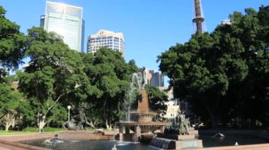 Sydney şehrinin Hyde Parkı 'ndaki tarihi çeşme dereleri mavi gökyüzüne ve modern kulelere bakıyor..