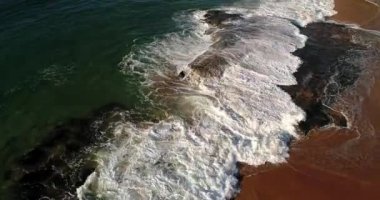 Temiz kum ve düz kaya Pasifik Okyanusu dalgaları tarafından tepeden aşağı doğru uçuyor..