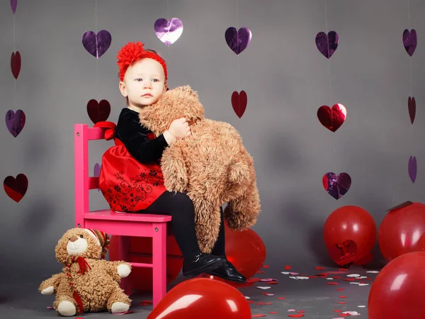 Retrato de blanco caucásico lindo adorable bebé niña niño sentado en una pequeña silla rosa con juguete oso en el estudio con vestido rojo y diadema, día de San Valentín de vacaciones — Foto de Stock