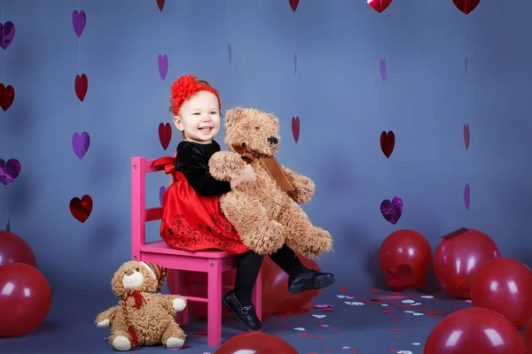 Potret putih Kaukasia lucu bayi perempuan kecil yang menggemaskan duduk di kursi merah muda kecil dengan mainan beruang di studio mengenakan gaun merah dan ikat kepala tersenyum bersenang-senang, liburan Hari Valentine — Stok Foto
