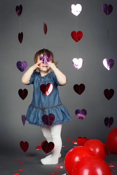 Potret lucu lucu lucu putih Kaukasia gadis kecil di studio dengan balon merah hati di latar belakang abu-abu membuat wajah bersenang-senang, Valentine liburan, konsep masa kanak-kanak bahagia — Stok Foto