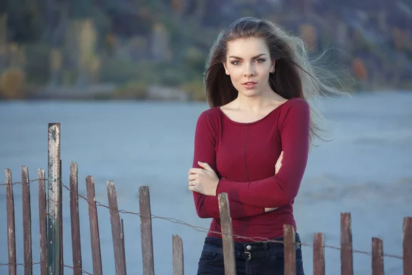 Portrait de songeur triste solitaire Caucasien jeune belle femme avec les cheveux longs désordonnés sur le vent jour extérieur sur la plage de rivage près de clôture en bois au coucher du soleil — Photo