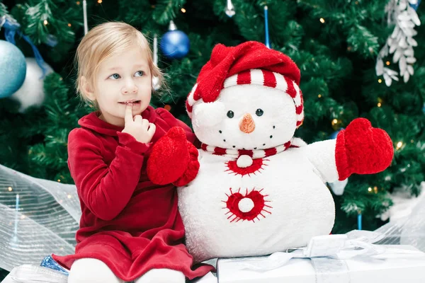 Portrait de bébé fille caucasienne souriante heureuse tout-petit avec les yeux bleus en robe rouge assis près de l'arbre de Nouvel An jouet bonhomme de neige, style de vie émotionnel Noël concept de vacances — Photo