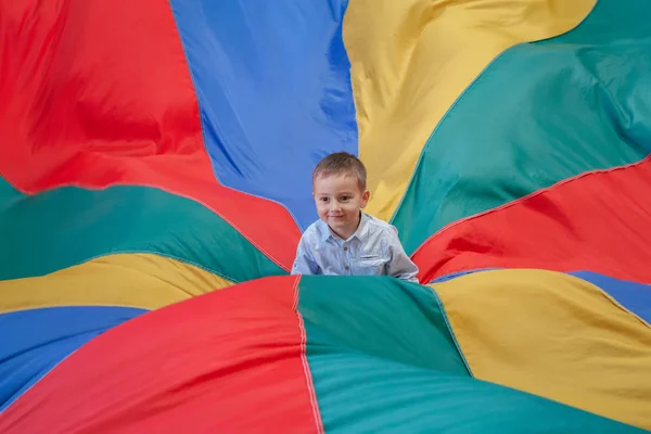 Retrato de niño blanco caucásico niño sentado en el centro del parque infantil paracaídas de arco iris celebrando su cumpleaños en la fiesta —  Fotos de Stock