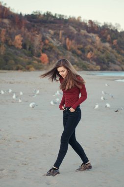 Beyaz martılar kuşlar arasında sonbahar sonbahar gününde açık kıyı sahilde günbatımı, yaşam tarzı doğal duygu atlama koşma kot pantolon bir genç kadın mutlu gülümseyen gülen portre heyecanlı