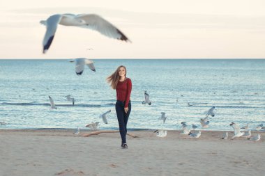 Beyaz martılar kuşlar arasında sonbahar sonbahar gününde açık kıyı sahilde günbatımı, yaşam tarzı doğal duygu atlama koşma kot pantolon bir genç kadın mutlu gülümseyen gülen portre heyecanlı