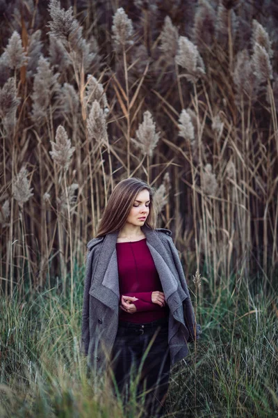 Portrait of pensive sad lonely Caucasian blonde young beautiful woman girl with long hair wearing jeans, coat jacket,  in forest field among large tall plants grass, looking away — Stock Photo, Image