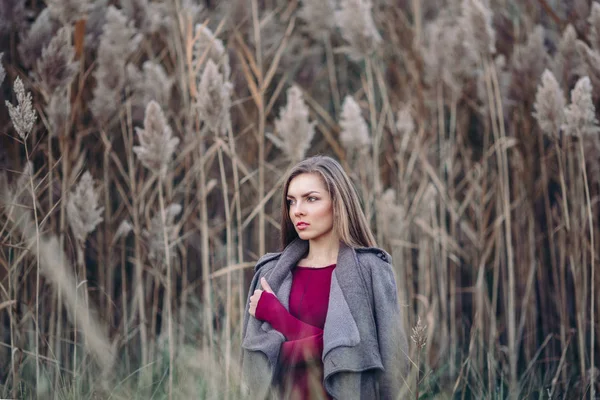 Portrait of pensive sad lonely Caucasian blonde young beautiful woman girl with long hair wearing jeans, coat jacket,  in forest field among large tall plants grass, looking away — Stock Photo, Image