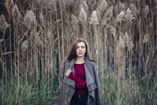 Portret van peinzende triest eenzaam Kaukasische blonde jonge mooie vrouw meisje met lang haar dragen van jeans, vacht jas, in bos veld onder grote hoge planten gras in de camera kijken — Stockfoto