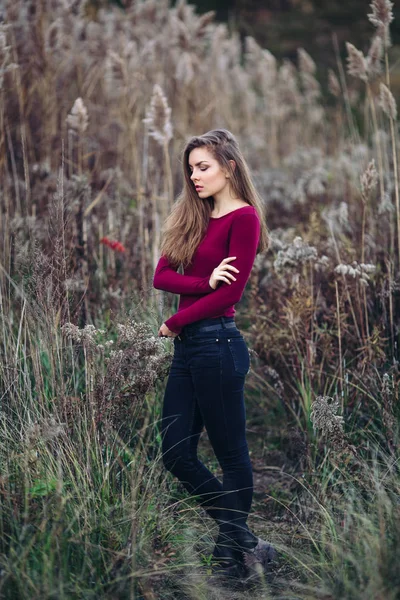 Portret van peinzende triest eenzaam Kaukasische blonde jonge mooie vrouw meisje met lang haar dragen van jeans, rood shirt, in bos veld onder grote hoge planten gras, op zoek weg — Stockfoto