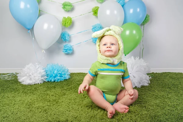 Retrato de bonito menino caucasiano adorável em feriado traje de coelho de Páscoa com orelhas grandes, vestido com roupas verdes onesie, sentado no tapete macio tapete fofo no estúdio no fundo branco — Fotografia de Stock