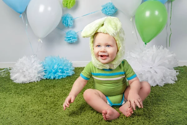 Retrato de lindo adorable bebé caucásico en vacaciones traje de conejo de Pascua con orejas grandes, vestido con ropa verde onesie, sentado en suave alfombra esponjosa alfombra en el estudio sobre fondo blanco — Foto de Stock