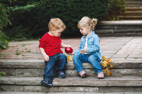 toddlers sitting together sharing  apple