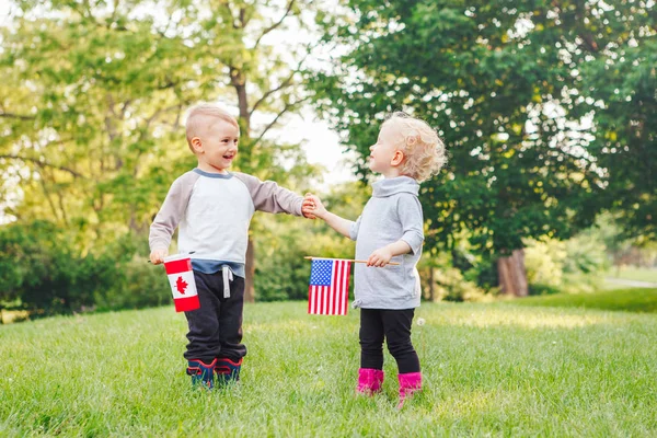 Девочка и мальчик улыбаются и машут американскими и канадскими флагами — стоковое фото