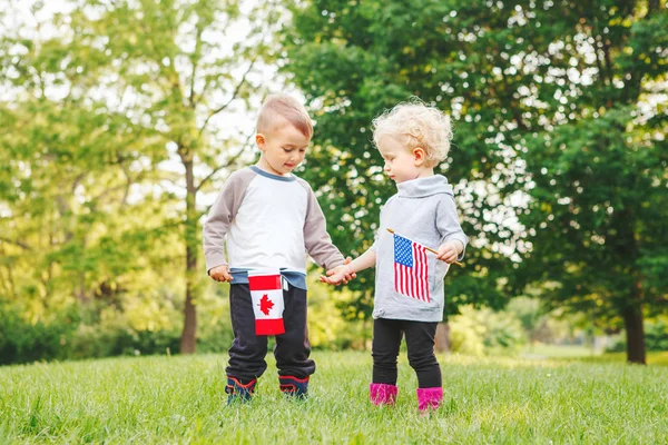 Девочка и мальчик улыбаются и машут американскими и канадскими флагами — стоковое фото