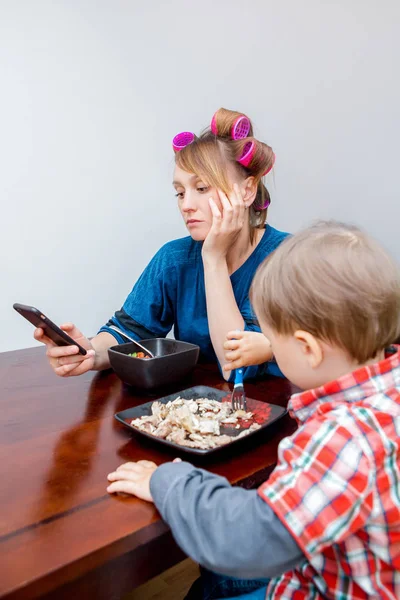 Домохозяйка с телефоном, пока сын ест — стоковое фото