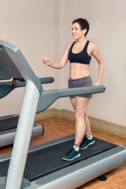 Güzel gülümseyen orta yaşlı beyaz beyaz esmer kadın spor salonunda egzersizleri yapıyor kısa saçlı portresi. Üst düzey Bayan yarış pisti kullanma