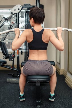 Güzel orta yaşlı beyaz beyaz esmer saçlı kadın spor salonunda egzersizleri yapıyor kısa portresi. Arkadan görüntülemek