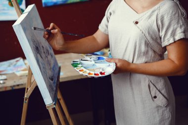 Portre genç orta yaş beyaz beyaz kadın sanatçının tuval üzerine akrilik boya ile resim çizim. Erkek holding Boya fırçaları ve Sanat Atölyesi palette eller. Yaşam tarzı etkinlik hobi kavramı