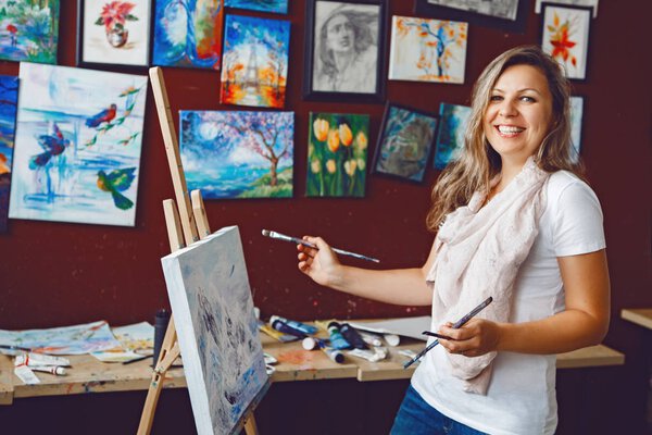 Portrait of young beautiful middle age white Caucasian woman artist drawing painting in art studio with acrylic paints on canvas. Lifestyle activity hobby concept