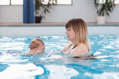 Beyaz beyaz yüzme havuzunda yüzmek için yeni doğan bebeği traning anne. Suya dalış bebeğim. Sağlıklı aktif yaşam tarzı. Aile aktivitesi ve erken geliştirme kavramı