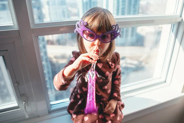 Muotokuva Valkoihoinen Tyttö Lapsi Istuu Ikkunalaudalla Kotona Puhaltaa Pilli Trumpetti — kuvapankkivalokuva