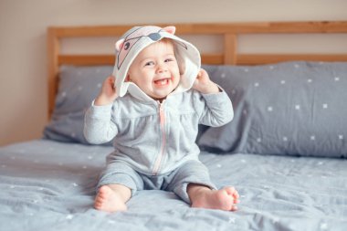 Portre sevimli sevimli Beyaz sarışın gülümseyen kız bebek yatak yatak odasında oturup fox kedi hayvan kukuleta ile gri pijama içinde mavi gözlü. Doğal duygu yüz ifadesi. 