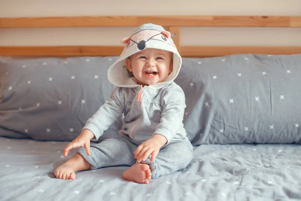 愛らしい白人金髪笑顔赤ちゃんとかわいい女の子の寝室のベッドの上に座っている狐猫動物フード付きグレーのパジャマで青い目の肖像画 自然な感情表情 — ストック写真