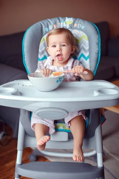 可爱的白种小孩的肖像坐在高高的椅子上吃麦片与勺子 每天的生活方式 坦诚真实的时刻 — 图库照片