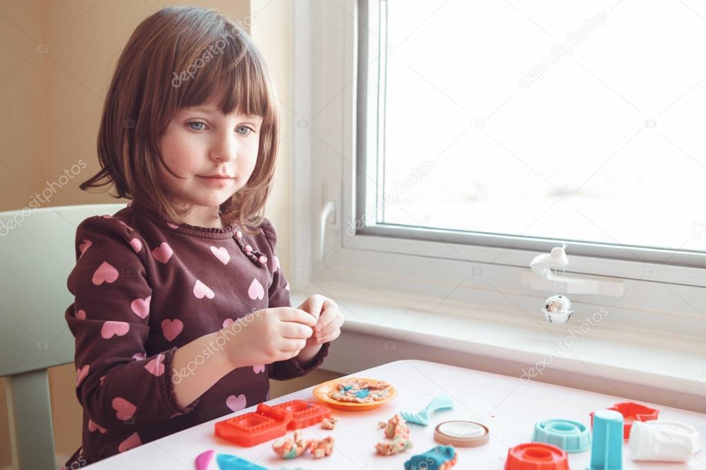 Portrait of cute white Caucasian preschooler girl playing plasticine playdough indoors at home. Early creativity brain development concept. Children activity. Fine motor skills.
