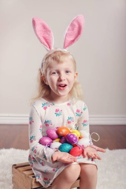 Paskalya bunny tavşan kulakları kapalı Studio ahşap kutu üzerinde oturan sevimli sevimli beyaz çocuk kız giyiyor. Çocuk holding tatil renkli kutluyor geleneksel kutsal Hıristiyan tatil yumurta 