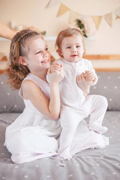 可爱可爱的白种白人女孩的肖像抱着小妹妹的膝盖膝上的婴儿 微笑的孩子们坐在一起睡在卧室里看着相机 兄弟姐妹的爱 — 图库照片