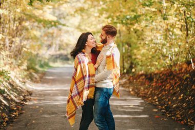 Aşık olan güzel bir çift. Güler yüzlü sevgili sarı battaniyeye sarılmış gülen sevgili sonbahar günü parkta sarılıyor. Beraberlik ve mutluluk. Otantik gerçek insanlar..