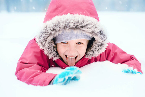 Cute adorable funny Caucasian excited girl child eating licking snow during cold winter snowy day. Kids outdoor seasonal activity. Happy candid authentic childhood lifestyle.