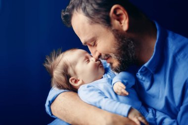 Orta yaşlı beyaz bir baba yeni doğmuş bebeği öpüyor. Erkek ebeveyn çocuğunu kucağına alıyor. Otantik yaşam tarzı dokunaklı bir an. Babamın aile hayatı konsepti. Klasik mavi 2020 renginde.. 