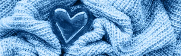 Closeup macro of classic blue knitted wool fabric with glass heart. Clothing texture monochrome background with wrinkles, folds. Valentine holiday love card. Web banner for website header. — Stock Photo, Image